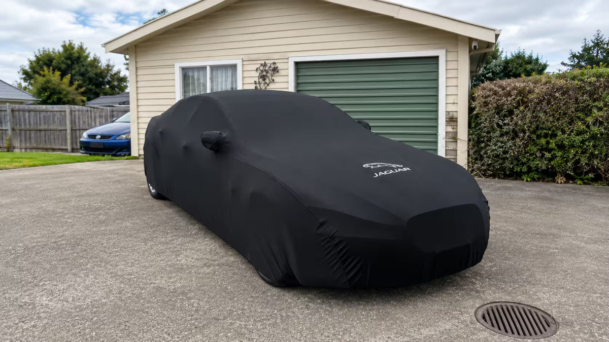 A car parked at a residential kerb at dusk, covered with a snug-fitting outdoor car cover.