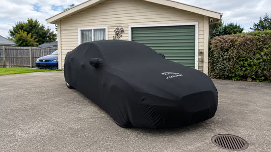 A car parked at a residential kerb at dusk, covered with a snug-fitting outdoor car cover.