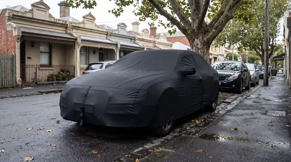 Black custom outdoor car cover strapped down on a sedan in a wet Melbourne terrace street